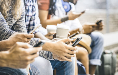 Midsection of friends using mobile phones while sitting outdoors