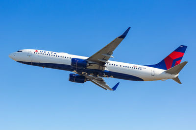 Low angle view of airplane flying against clear blue sky