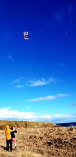 Rear view of men flying kite against blue sky