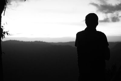 Rear view of silhouette man standing on rock against sky