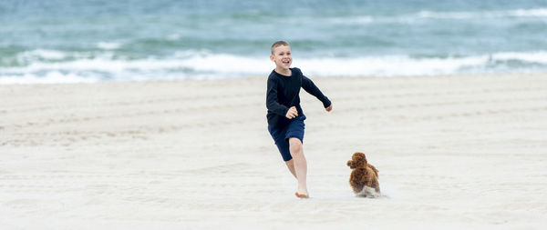 Full length of boy running with dog on beach