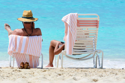 Rear view of male friends sitting on chairs at beach