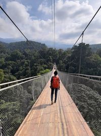 Rear view of man walking on footbridge against sky