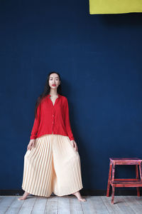 Portrait of young woman standing against wall