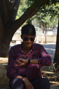 Young man wearing sunglasses sitting on tree