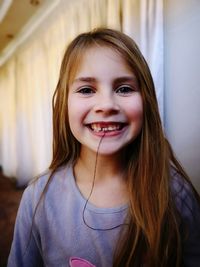 Portrait of cute smiling girl with thread tied on her tooth at home