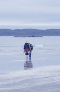 Full length of brother and sister standing on shore at beach against sky