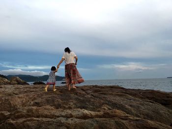Rear view of woman with daughter walking on rock formations by sea