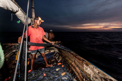 Rear view of man in boat in sea against sky during sunset