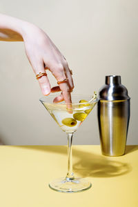 Woman dips finger with rings in glass of martini cocktail with olives