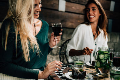 Smiling young woman drinking glass while sitting at cafe