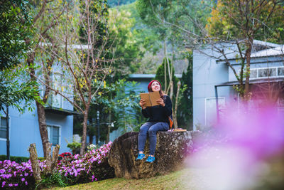 Woman holding book while sitting on stone