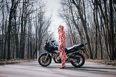 Man covered in red fabric while standing by motorcycle against bare trees