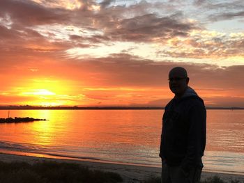 Portrait of man standing at beach against sky during sunset