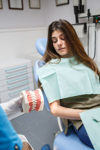 Professional doctor demonstration process of healthy teeth brushing to young woman sitting in chair.