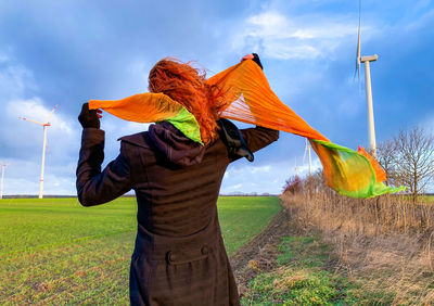 Woman holding textile while standing on agricultural field against sky