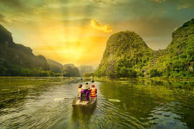 People on boat in lake against sky during sunset