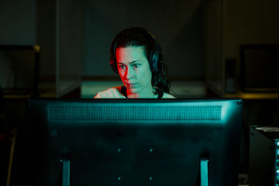 A woman with an intense gaze works at desktop computer in dark room