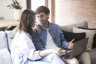 Friends using laptop while sitting on sofa at home