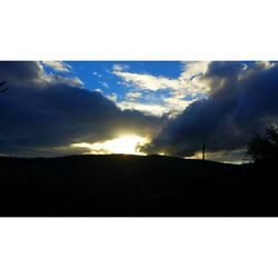 Scenic view of landscape against cloudy sky at sunset