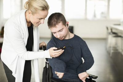 Female caretaker assisting disabled man in using mobile phone at home