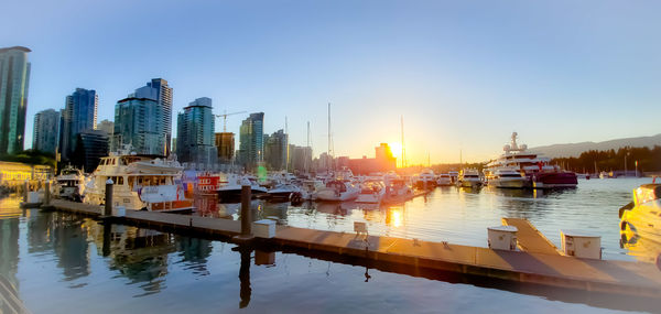 Sailboats moored on ocean inlet by urban buildings against clear sunset sky.