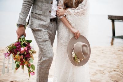 Midsection of bride and bridegroom standing at beach