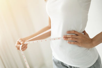 Midsection of woman measuring waist at home