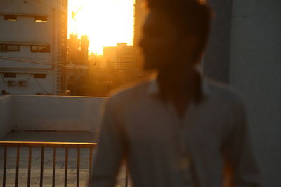 Man standing by railing against buildings in city at sunset