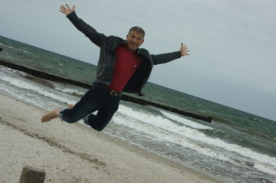 Portrait of playful mature man jumping with arms outstretched at beach