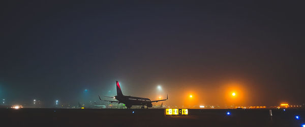 Airplane on airport runway against sky at night