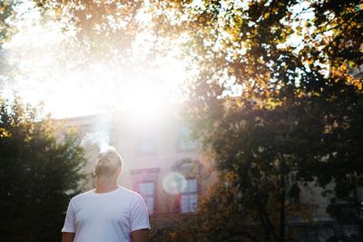 Rear view of man standing by trees against bright sun