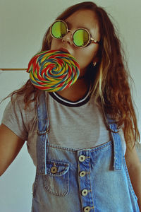 Young woman eating lollipop while standing against wall