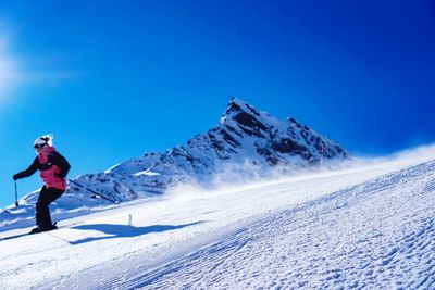 Woman skiing on snowcapped mountain against blue sky