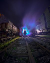 Man on railroad tracks against sky at night