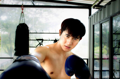 Portrait of shirtless man punching at gym