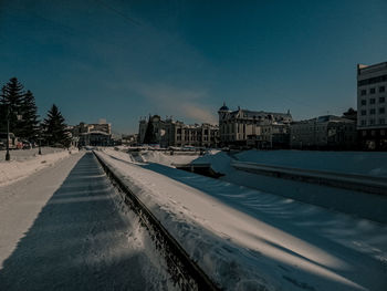Road by buildings in city against clear blue sky
