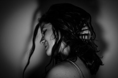 Side view of smiling young woman with hand in hair by wall