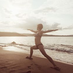 Full length of woman doing yoga at beach against sky