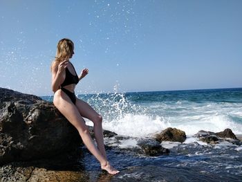 Young woman on rock in sea against sky