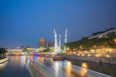 Illuminated city by river against clear sky at night