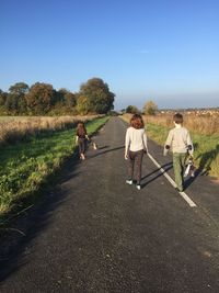 Rear view of siblings walking on country road against sky
