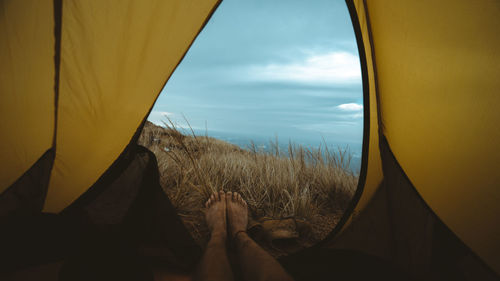 Low section of man relaxing in tent against blue sky