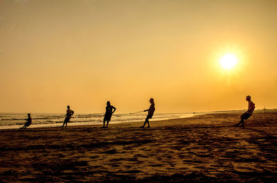 Silhouette people playing at beach against clear sky during sunset