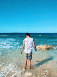 Rear view of man standing on beach against clear blue sky