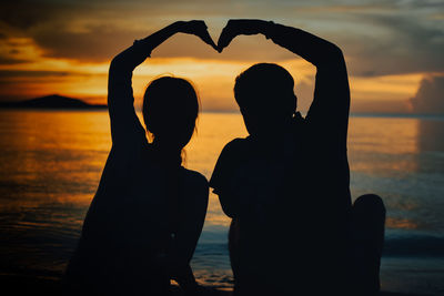 Silhouette couple at beach against sky during sunset