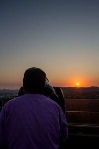 Rear view of man looking at sea against sky during sunset