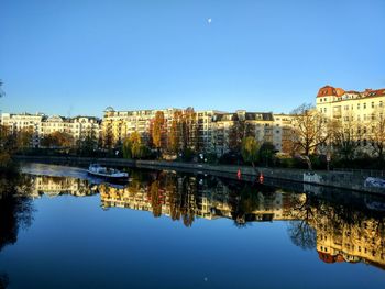 Reflection of buildings in river against clear blue sky