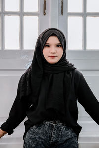 Portrait of young woman standing against wall
