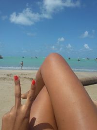 Low section of woman relaxing on beach against sky